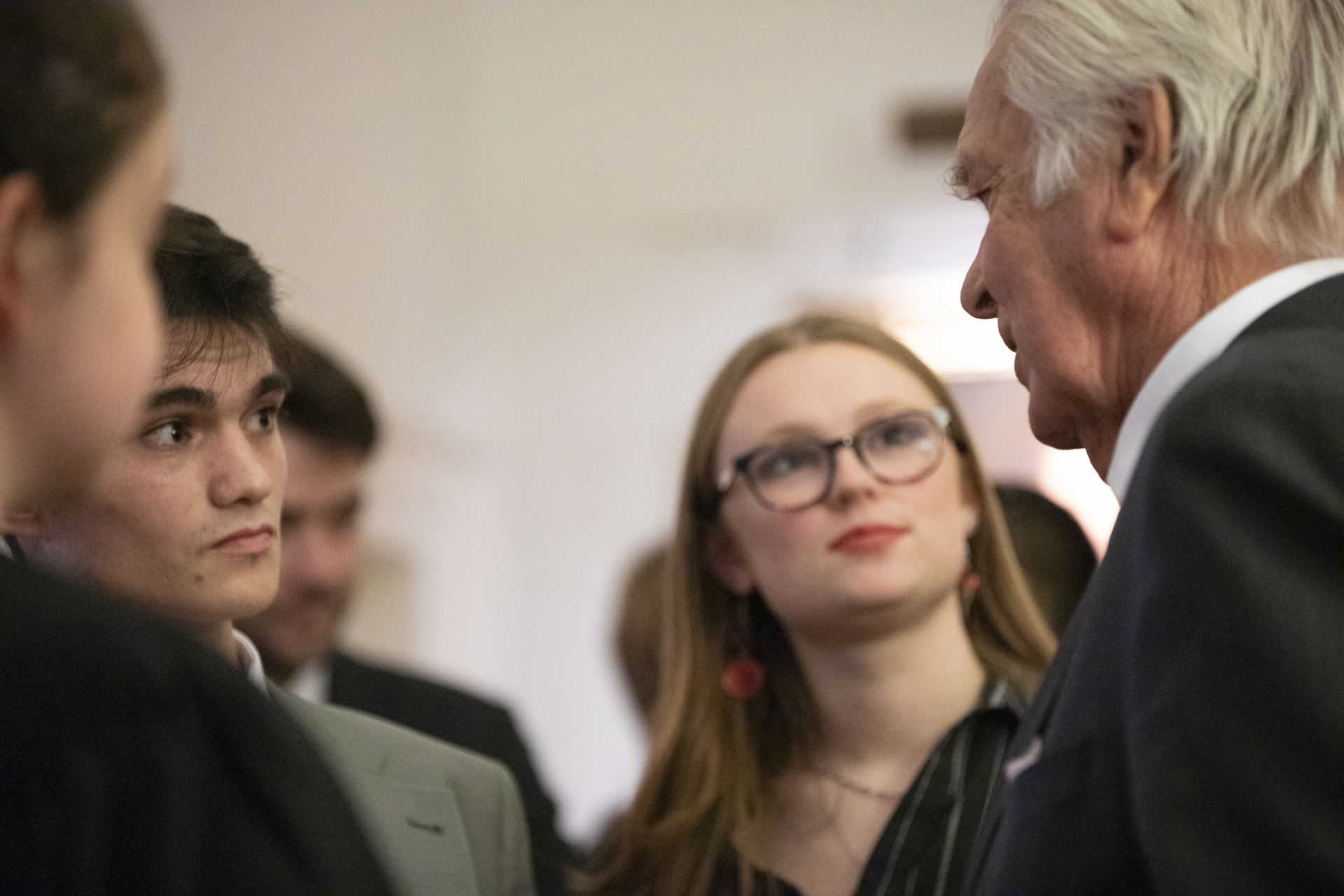 An older man (Lord Owen) speaks to a small group of students at a reception.